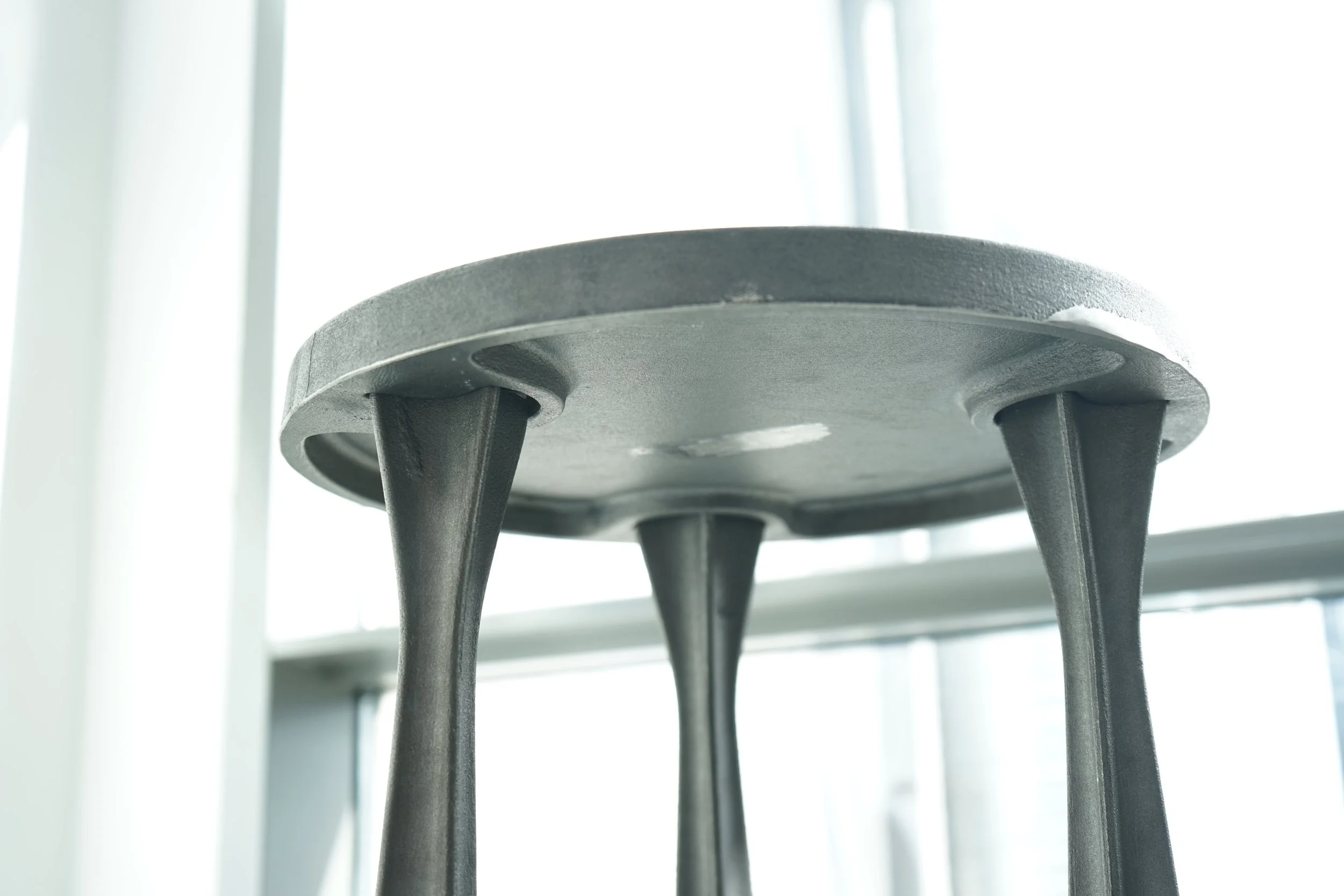 Close-up of a black metal chair leg and its round base, with a bright window in the background.