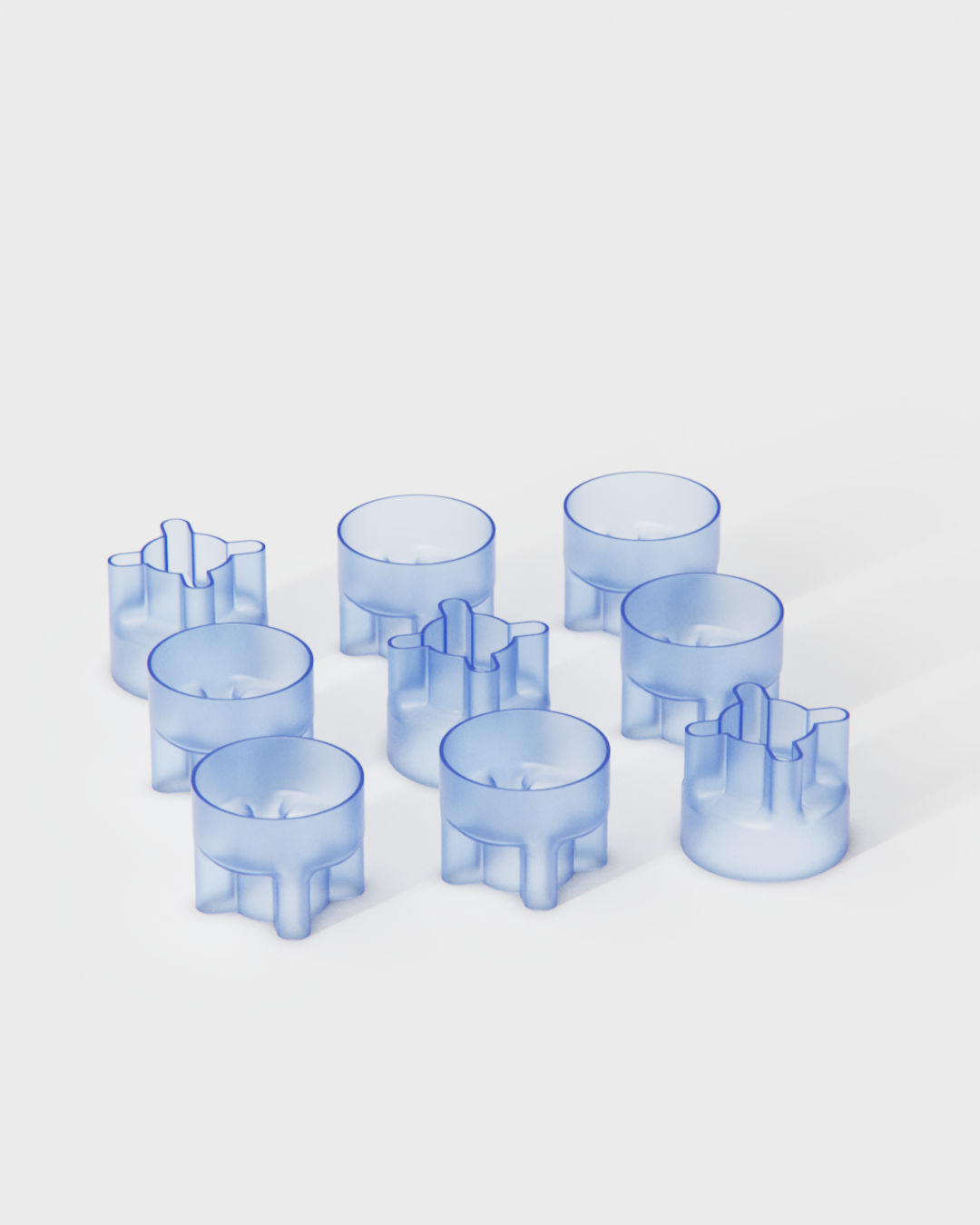 Nine blue plastic cookie cutters arranged on a white surface, with four having a circular shape and five having a shape resembling a cross or windmill.