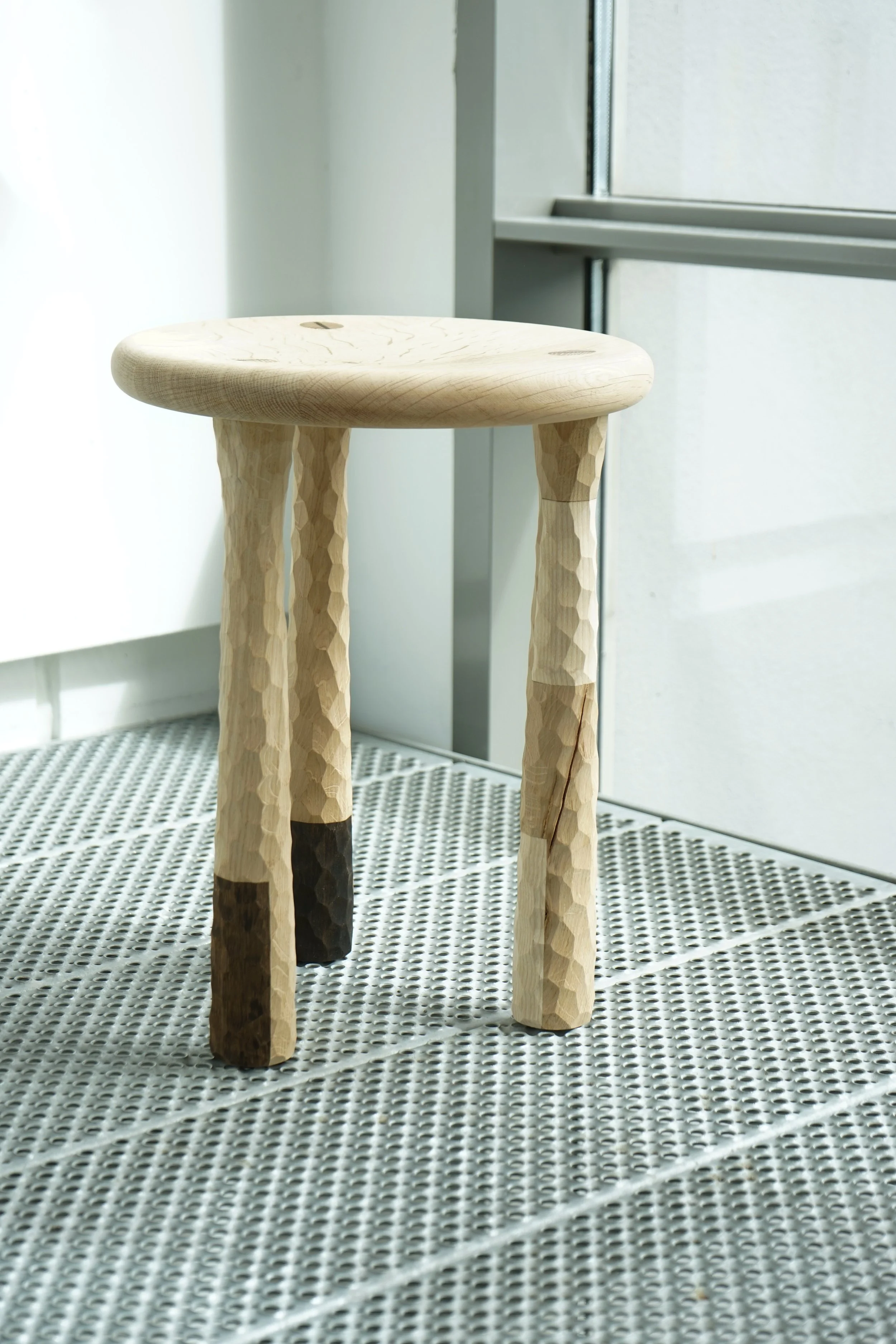 Wooden stool with textured, bumpy legs, located near a window with natural light.