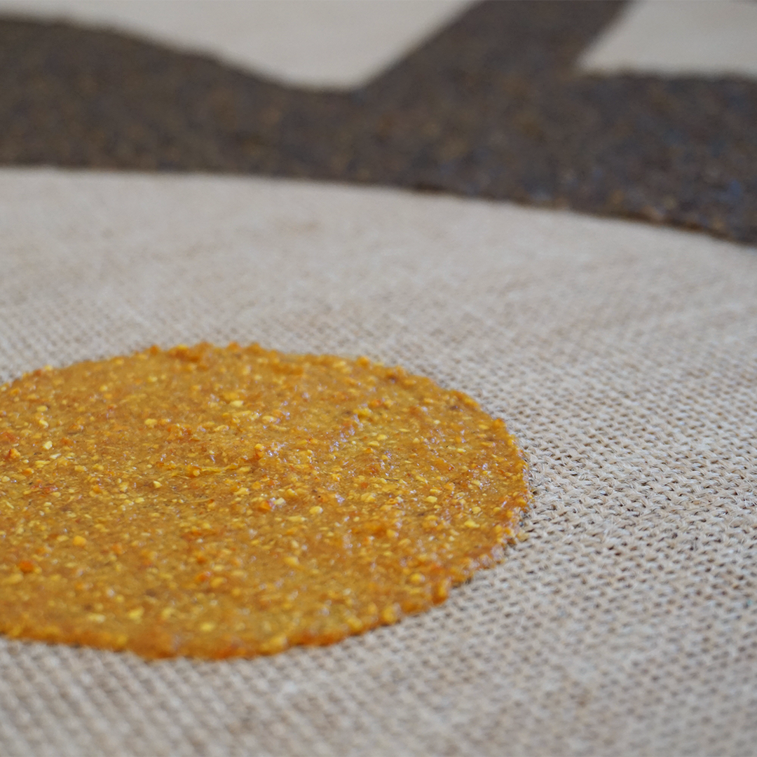 A close-up of a round, flat orange food item with a textured surface on a beige fabric surface.