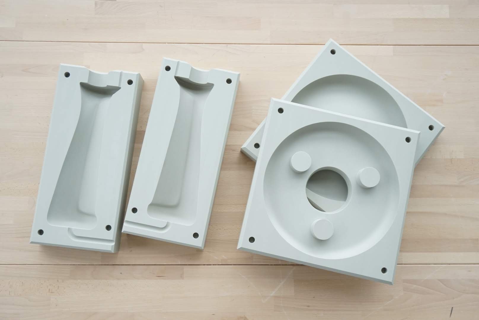Four white plastic electrical box components on a light wooden surface, two rectangular boxes with dimples on one side, and two square boxes with circular indentations and protruding knobs.