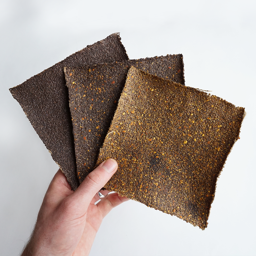 Hand holding three sheets of beef jerky with different seasonings, against a white background.