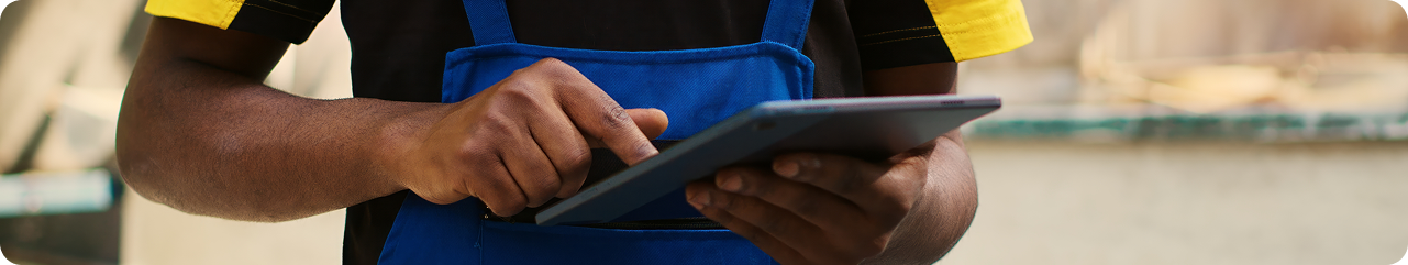 Person wearing a blue apron and yellow and black shirt using a tablet outdoors with blurred background