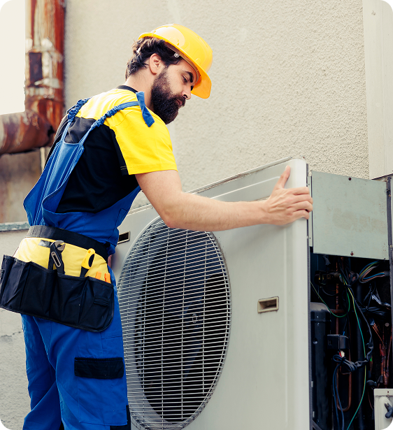 A technician in a yellow helmet and blue uniform working on an outdoor air conditioning unit.
