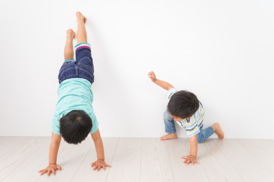 Zwei Kinder spielen und üben Lieblingspositionen auf dem Boden vor einer weißen Wand.
