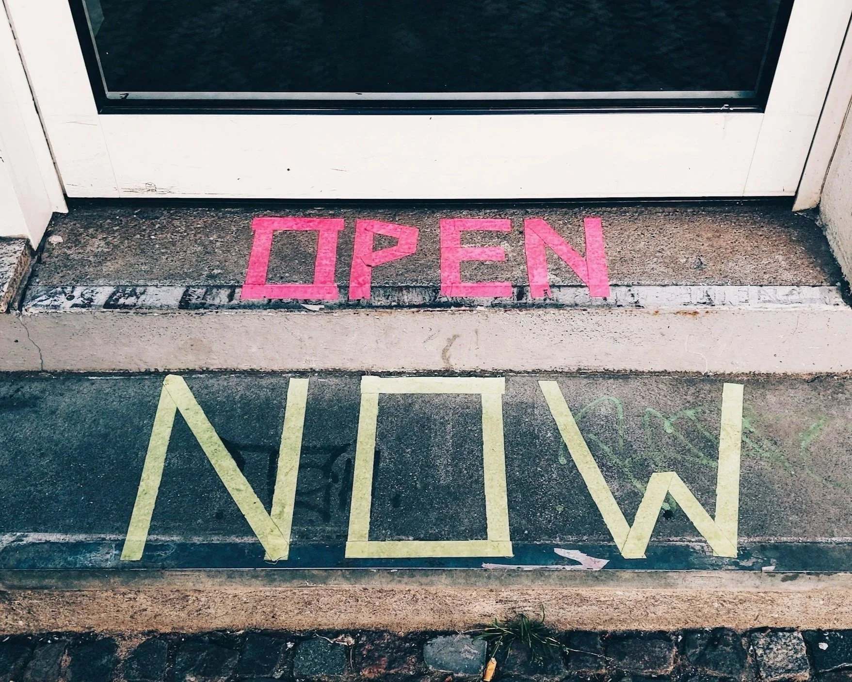 Doorstep with the word 'OPEN' painted in pink above the door and the word 'MAIN' painted in yellow on the concrete step.