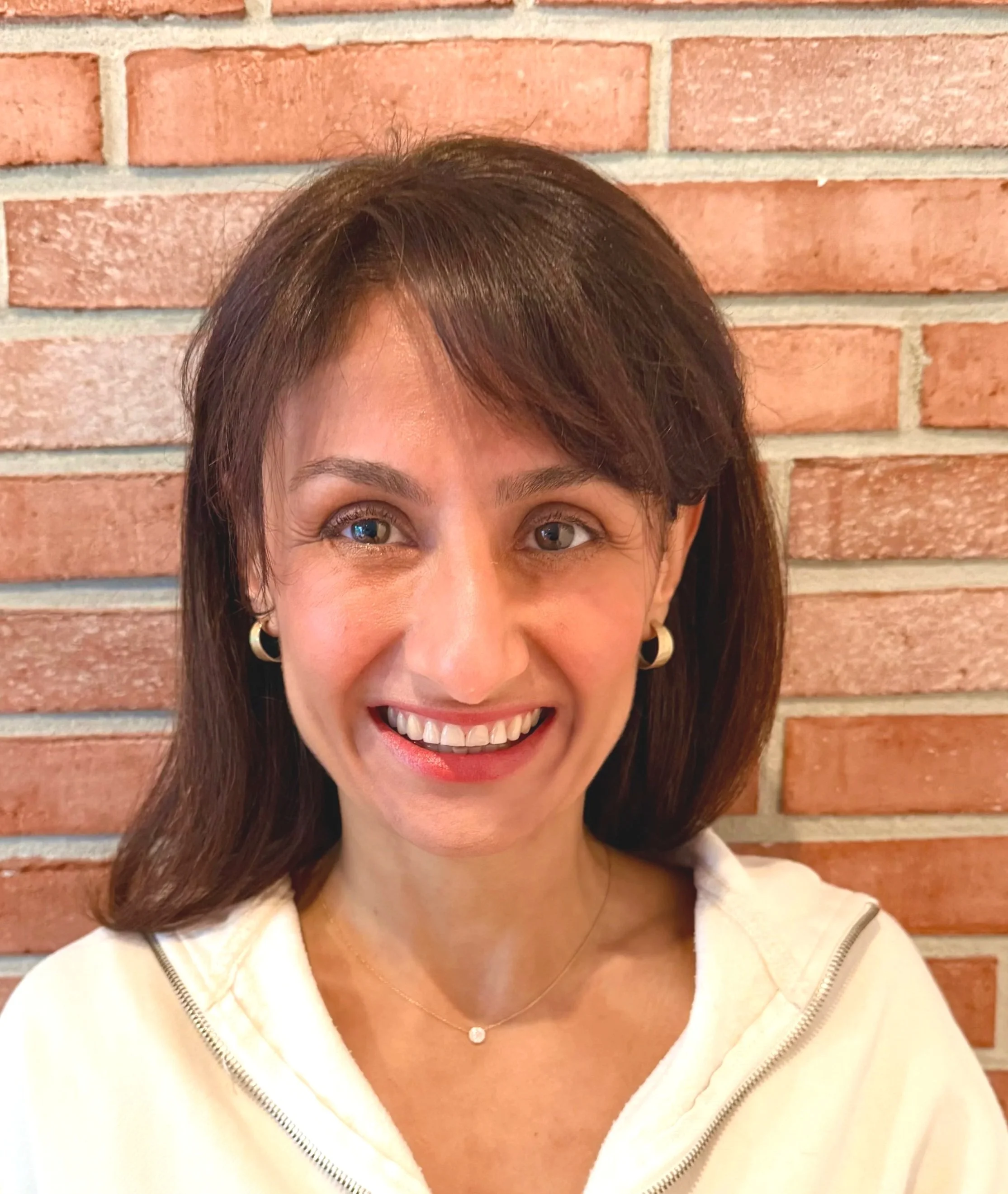 Close-up of a smiling woman's face showing her eyes, nose, and mouth, with a brick wall in the background.