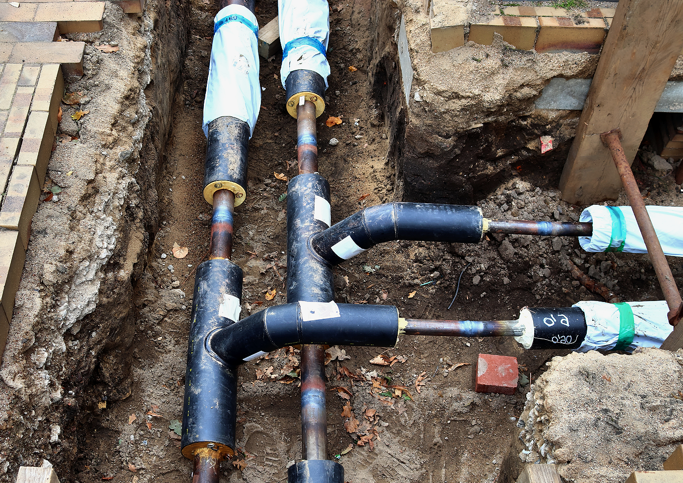 Installation von Wasserleitungen in einer Baugrube, mit Rohren und Verbindungen, teilweise noch eingepackt.
