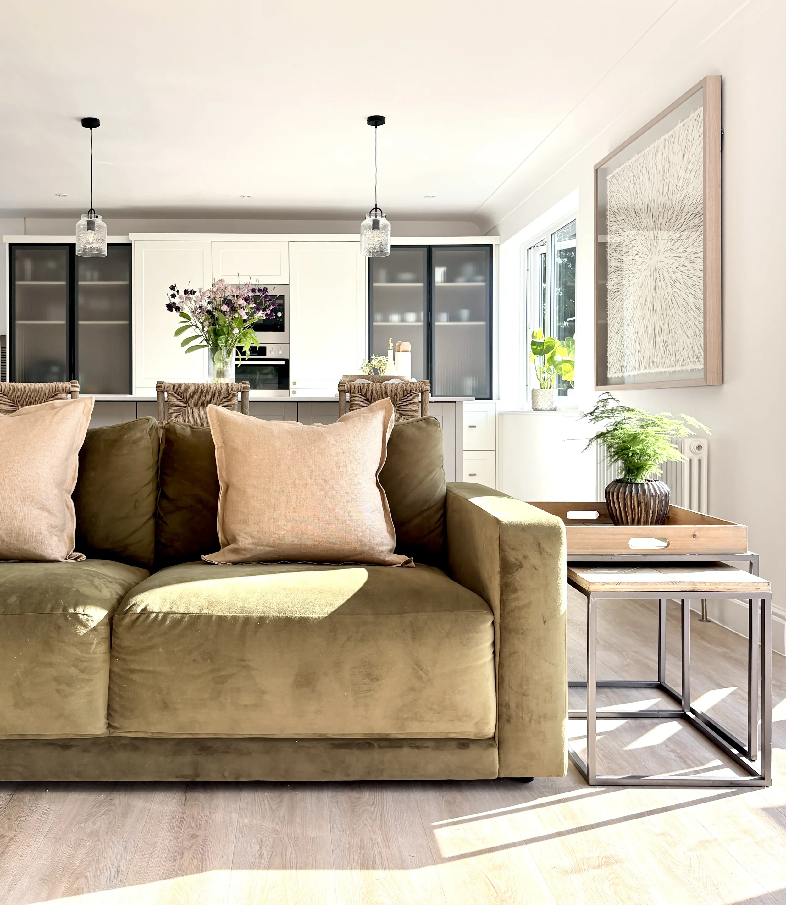 Living room with beige sofa, wooden side table, large abstract art on white wall, and sunlight streaming through window.