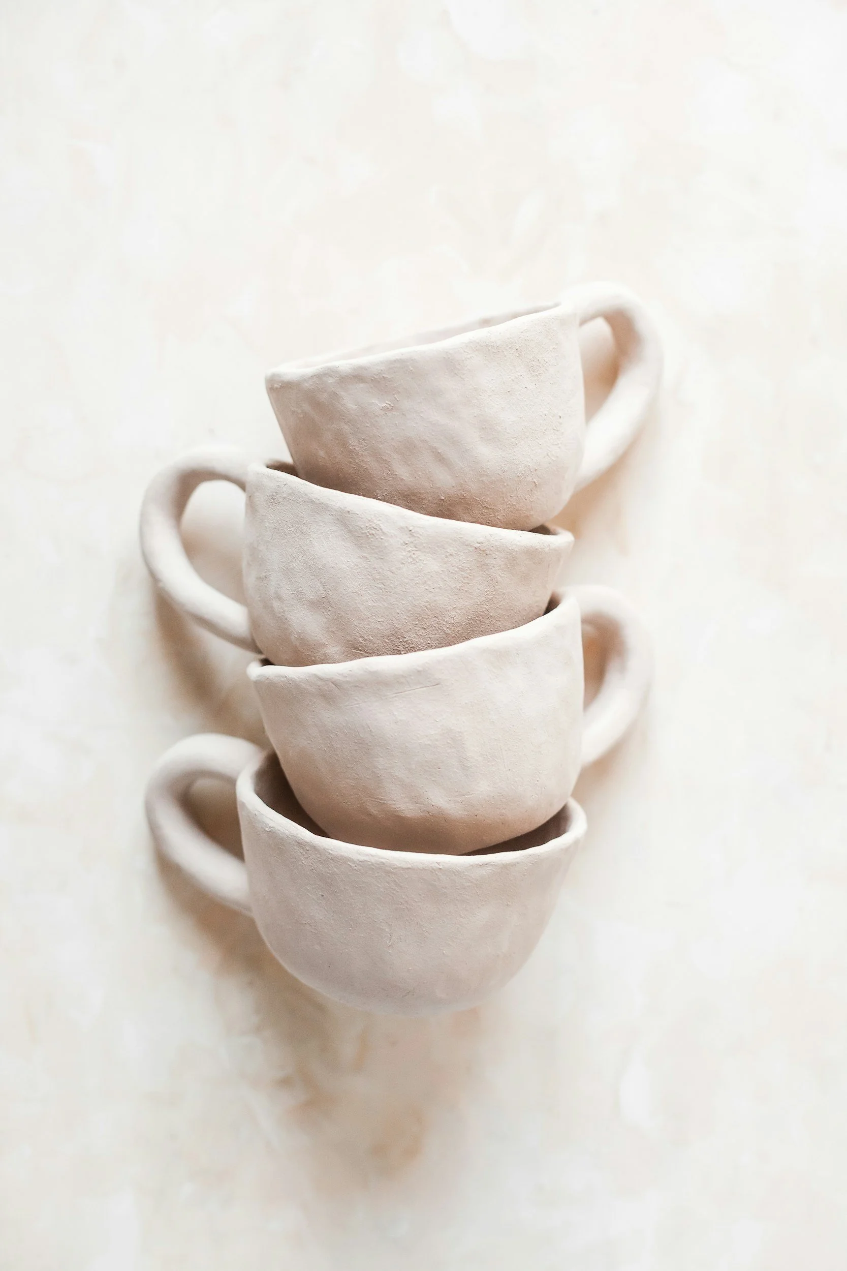 Stacked white ceramic cups with a textured surface, arranged on a light background.