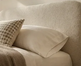 Close-up of a neatly made bed with cream-colored pillows and a textured throw blanket in a bedroom.