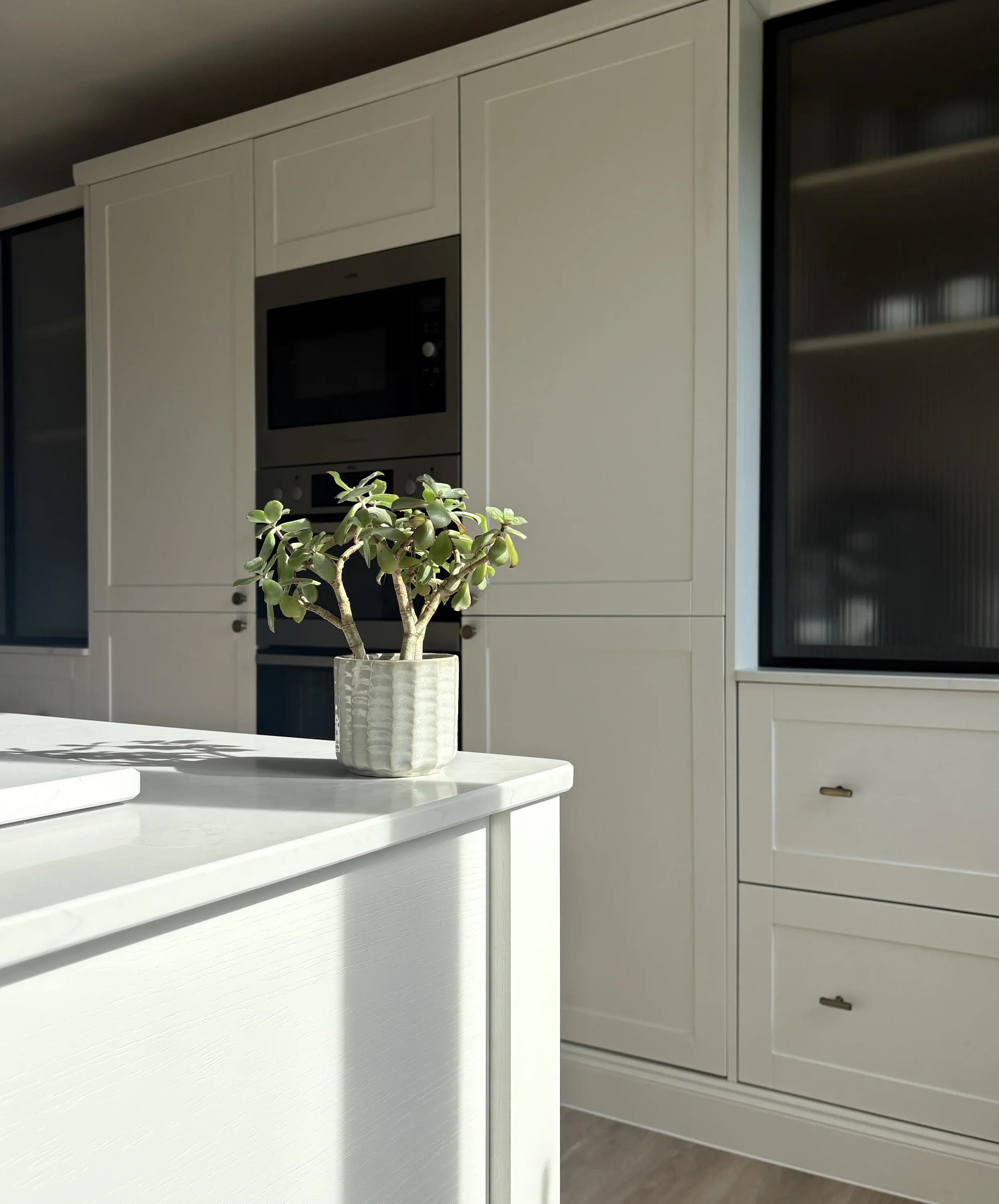 Bespoke kitchen design, modern shaker with marble worktop, brushed brass hardware, and a fresh green succulent plant.