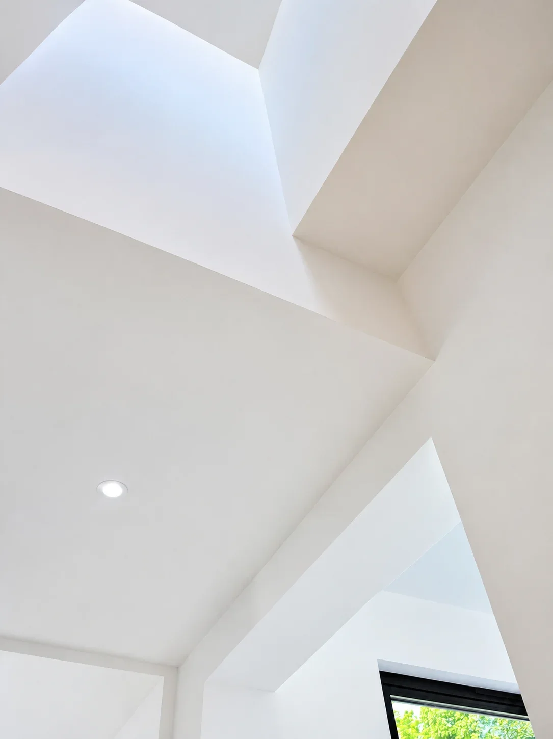 White modern architectural ceiling with skylights and a small window showing greenery outside.