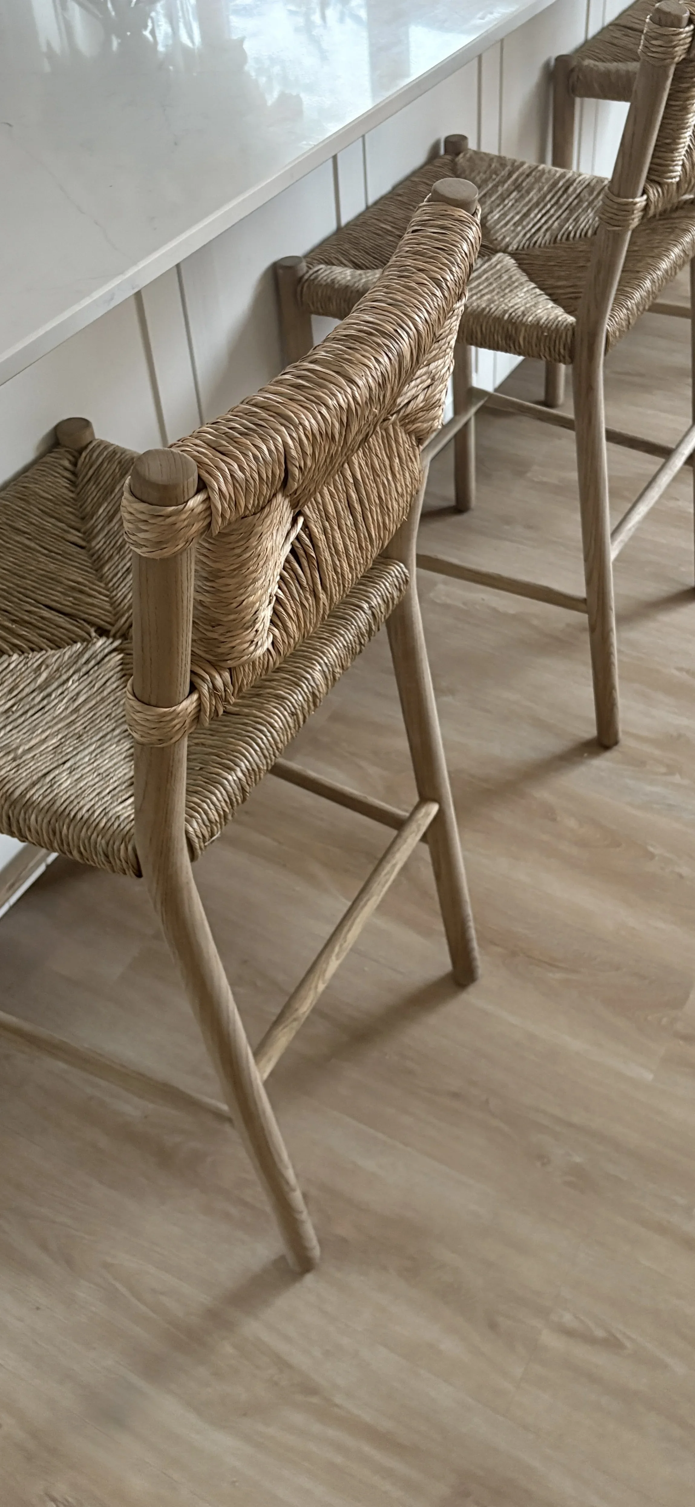 Woven rattan bar stools positioned at a contemporary kitchen island, showcasing natural materials, handcrafted textures and a warm neutral interior palette