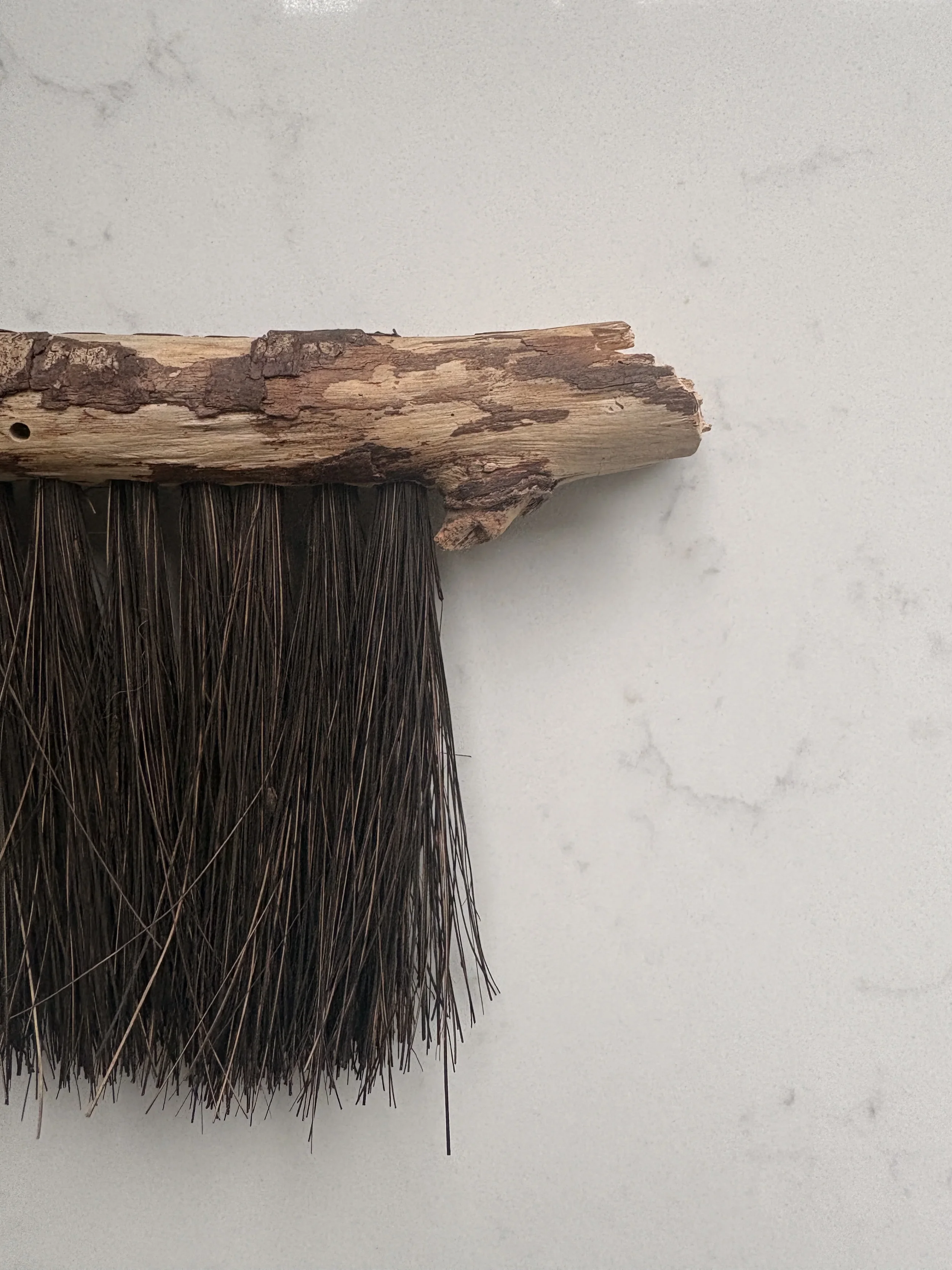 Close-up of a handcrafted natural fibre wall hanging with weathered wood detailing against a light stone surface, showcasing organic textures in a contemporary luxury interior