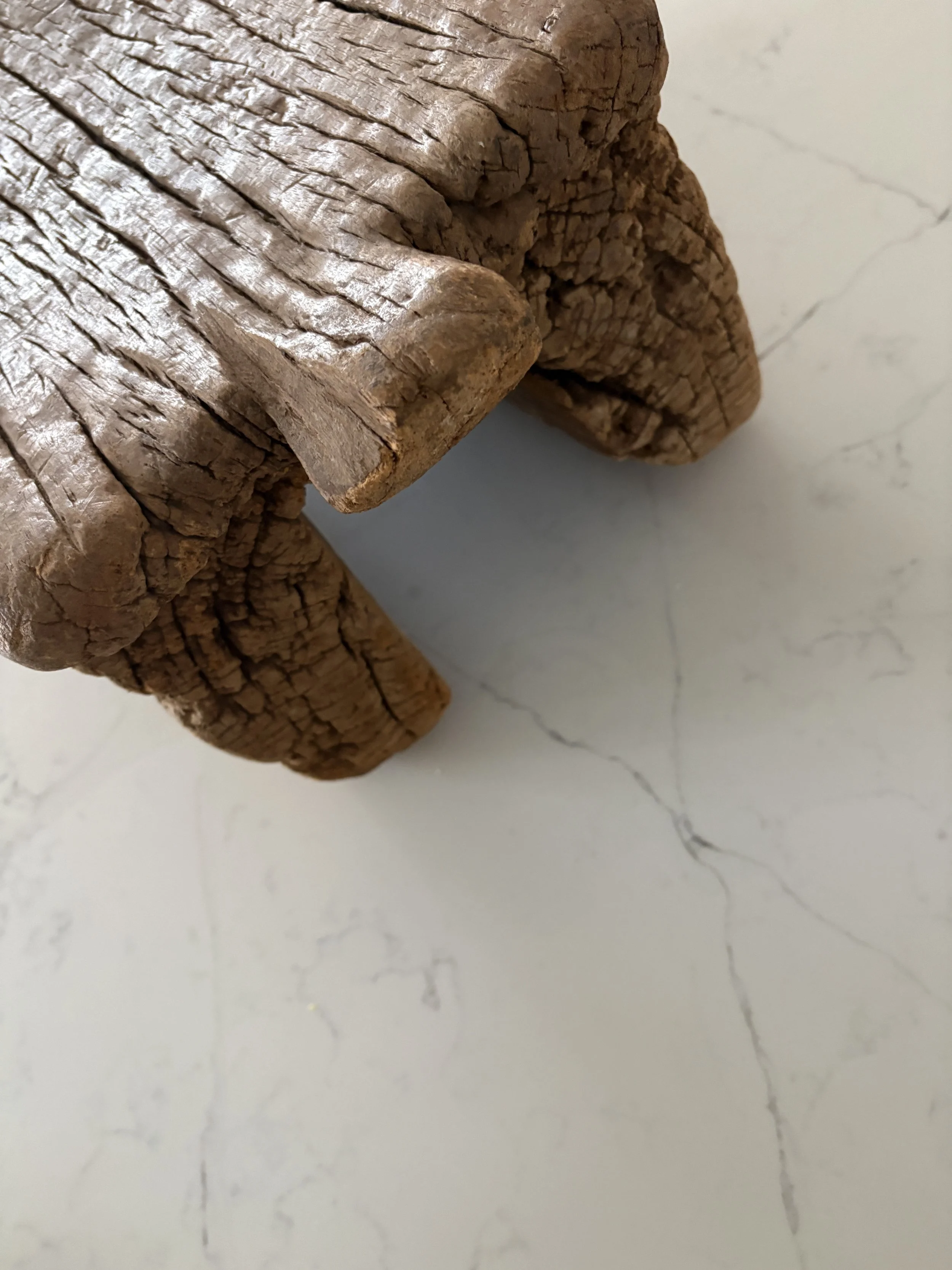 Close-up view of a wooden sculpture or furniture with detailed grain and aged surface against a light background.