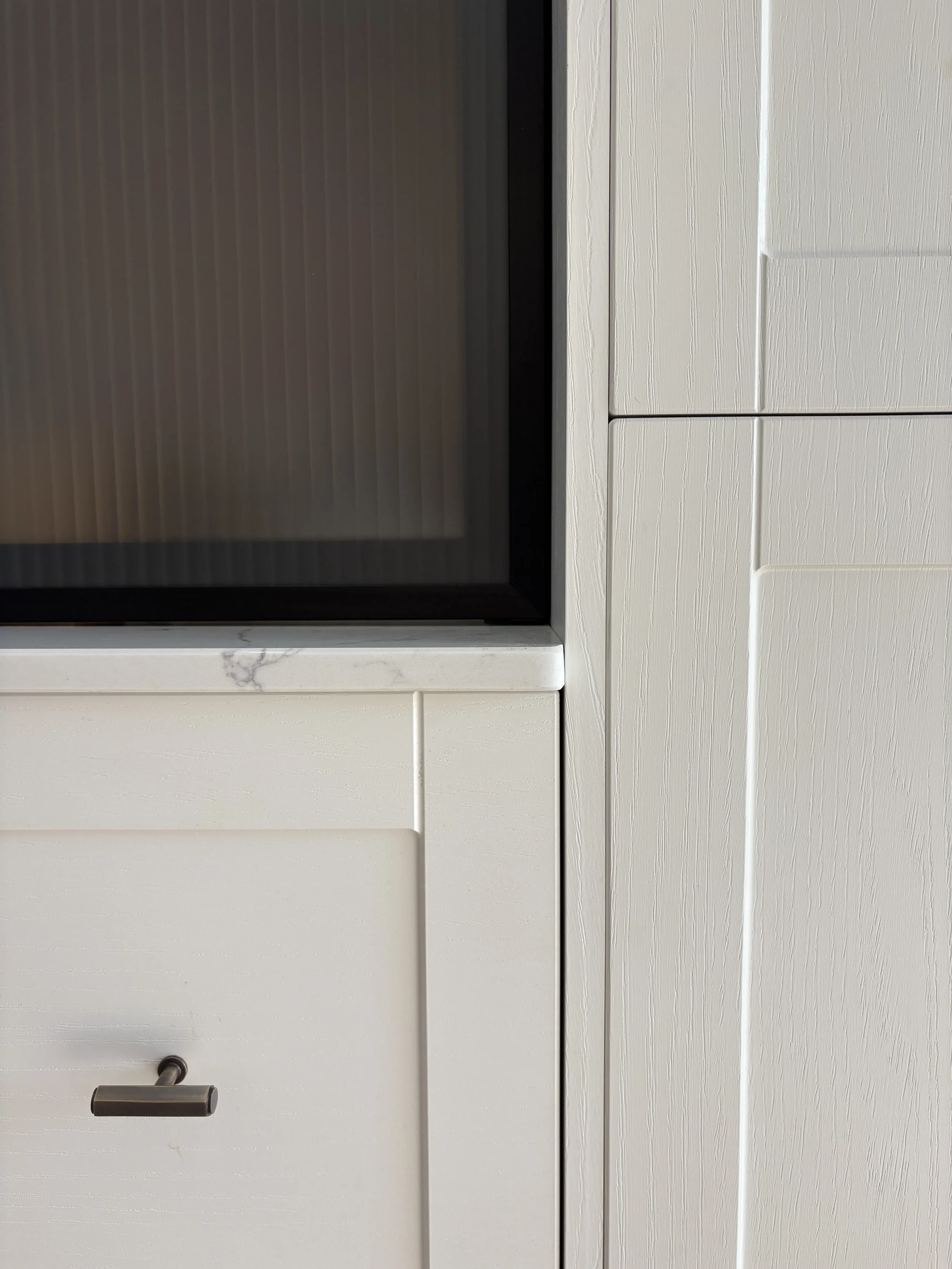 Close-up of bespoke kitchen joinery featuring painted cabinetry, fluted glass doors, marble shelving and bronze hardware in a contemporary luxury kitchen