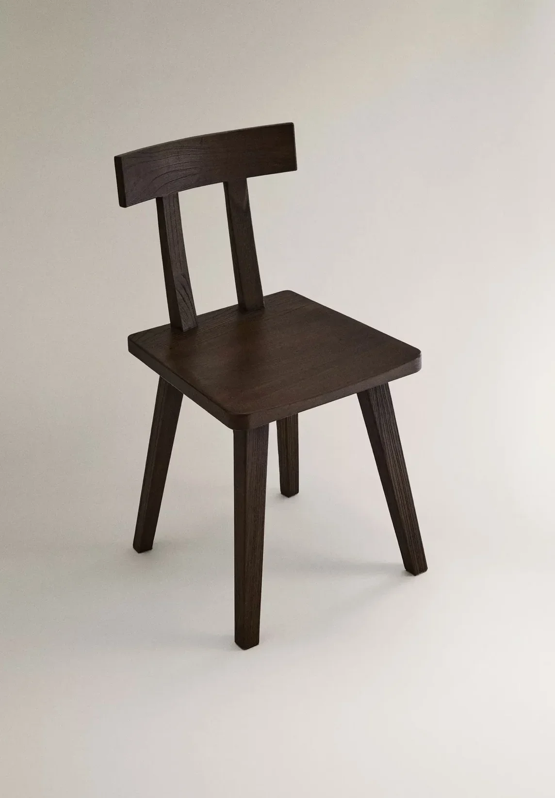A small dark wooden chair with a slatted back and four angled legs, set against a plain light-colored background.