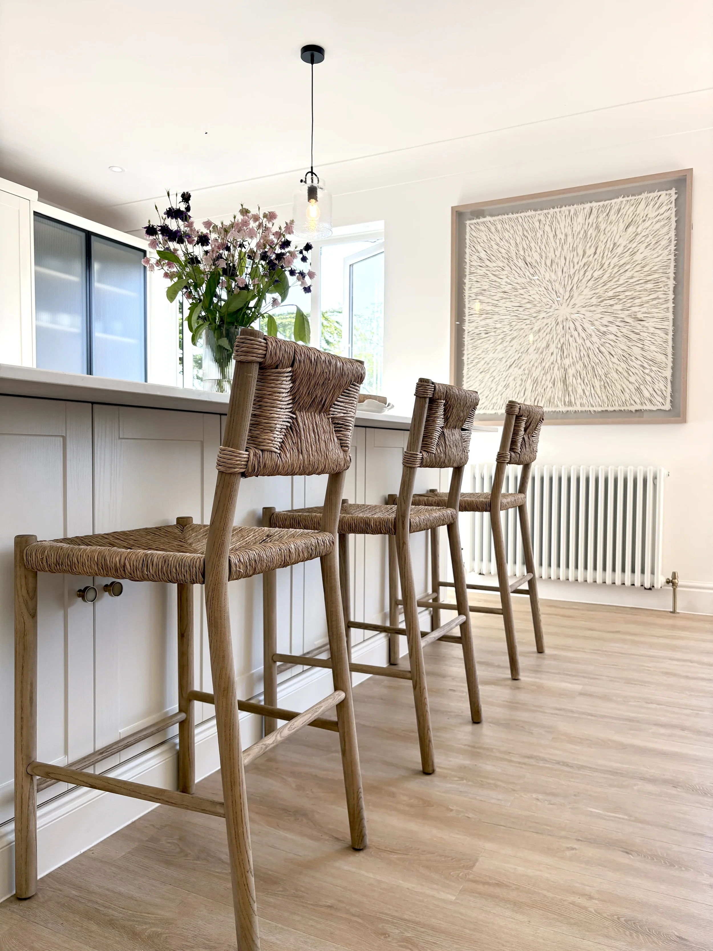Bespoke kitchen island with woven bar stools and natural material finishes, designed to create a functional and sociable gathering space within a contemporary family home.