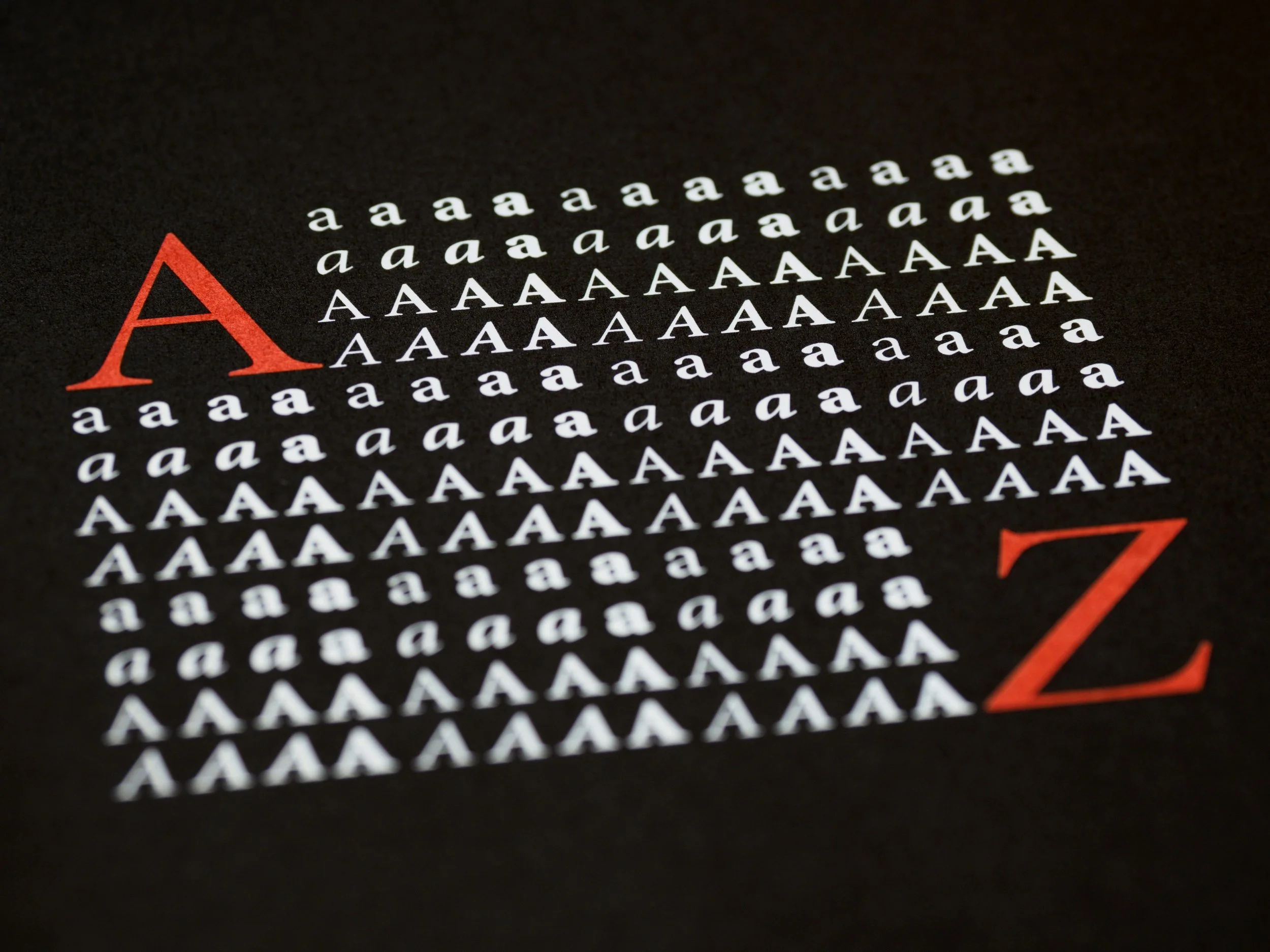 Close-up of a black sheet with multiple repetitions of the lowercase letter 'a' in white and the uppercase letter 'A' in white, forming rows and columns. There is a large red uppercase 'A' and a large red uppercase 'Z' partially visible.