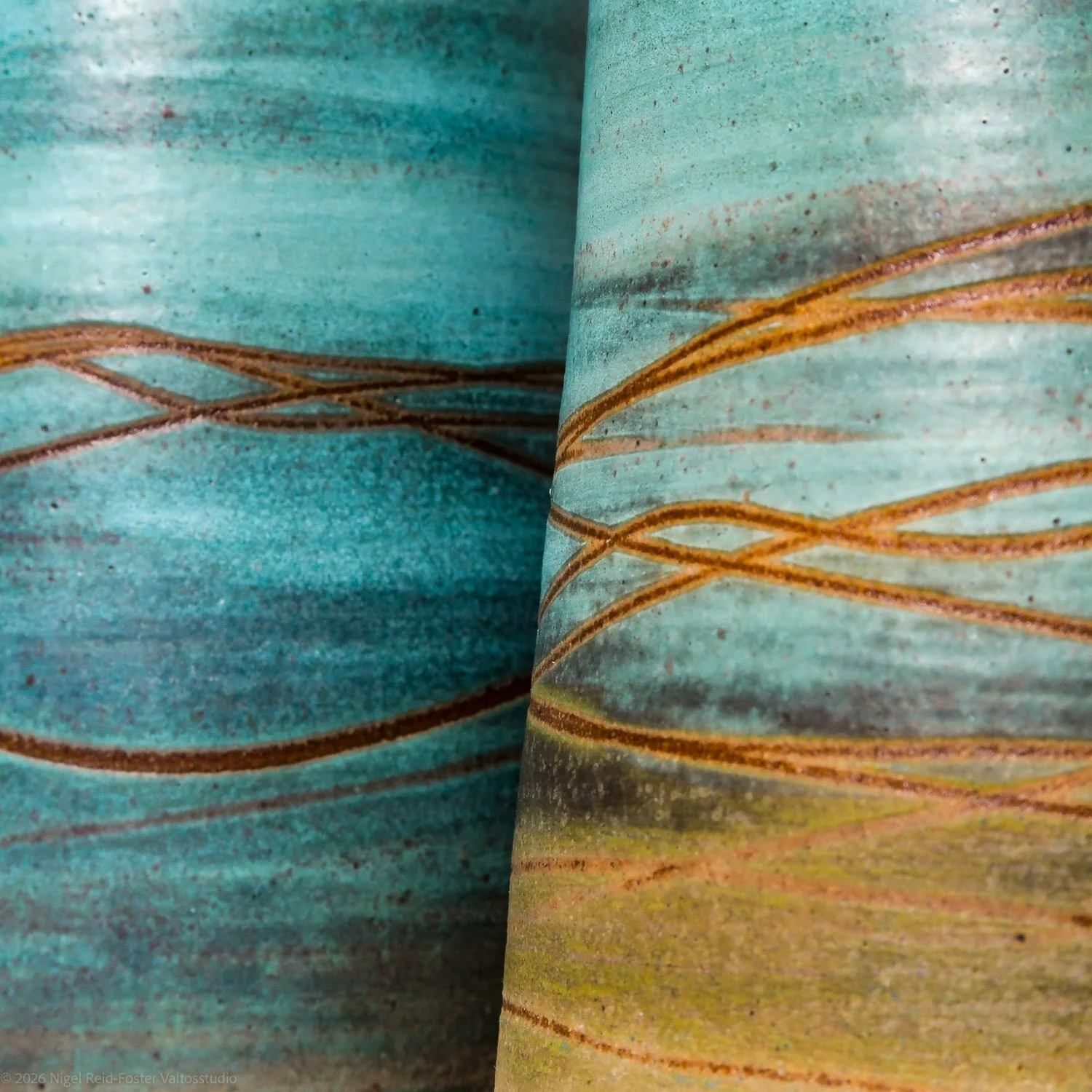 Close-up of textured ceramic vases with horizontal brown lines, in shades of blue, green, and yellow.