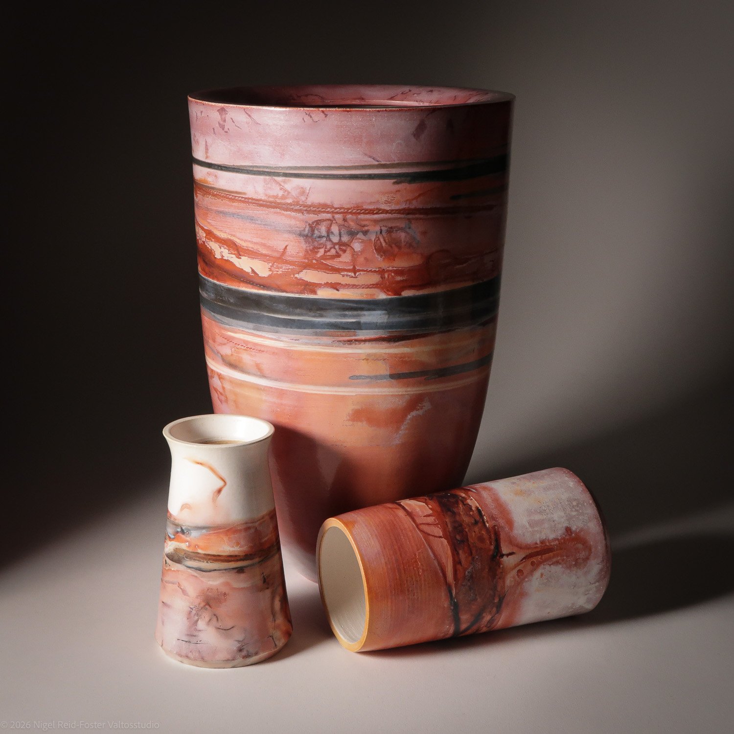 Three ceramic vases with marble-like patterns in shades of pink, peach, white, black, and gray, arranged against a dark, gradient background.