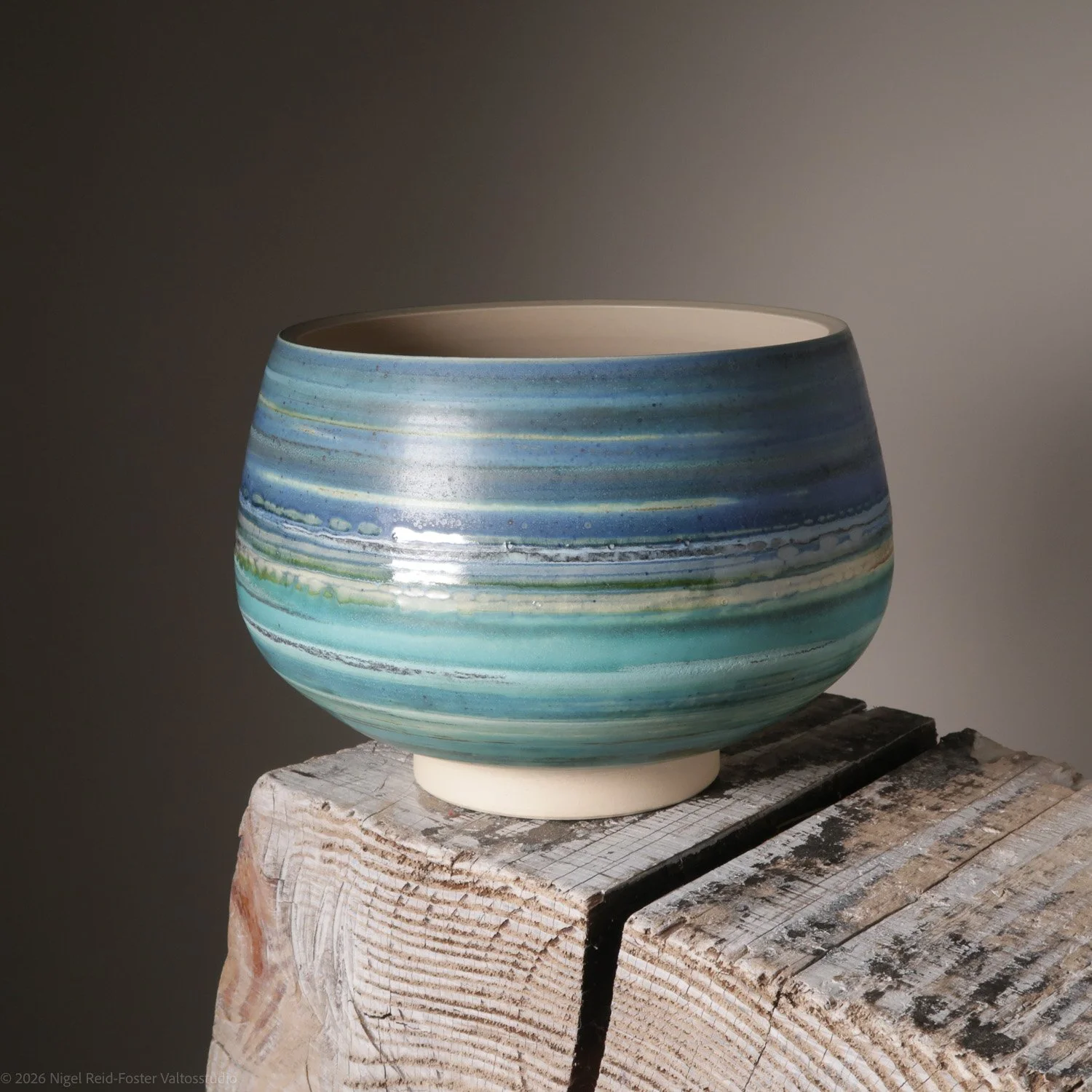 A ceramic bowl with blue and green horizontal striped glaze on a weathered wooden surface.
