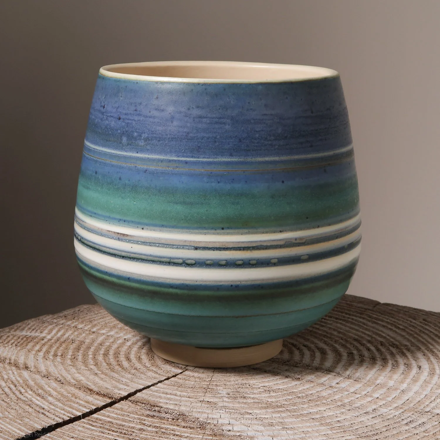 Colorful ceramic vase with blue, green, and white horizontal stripes on a wooden surface.