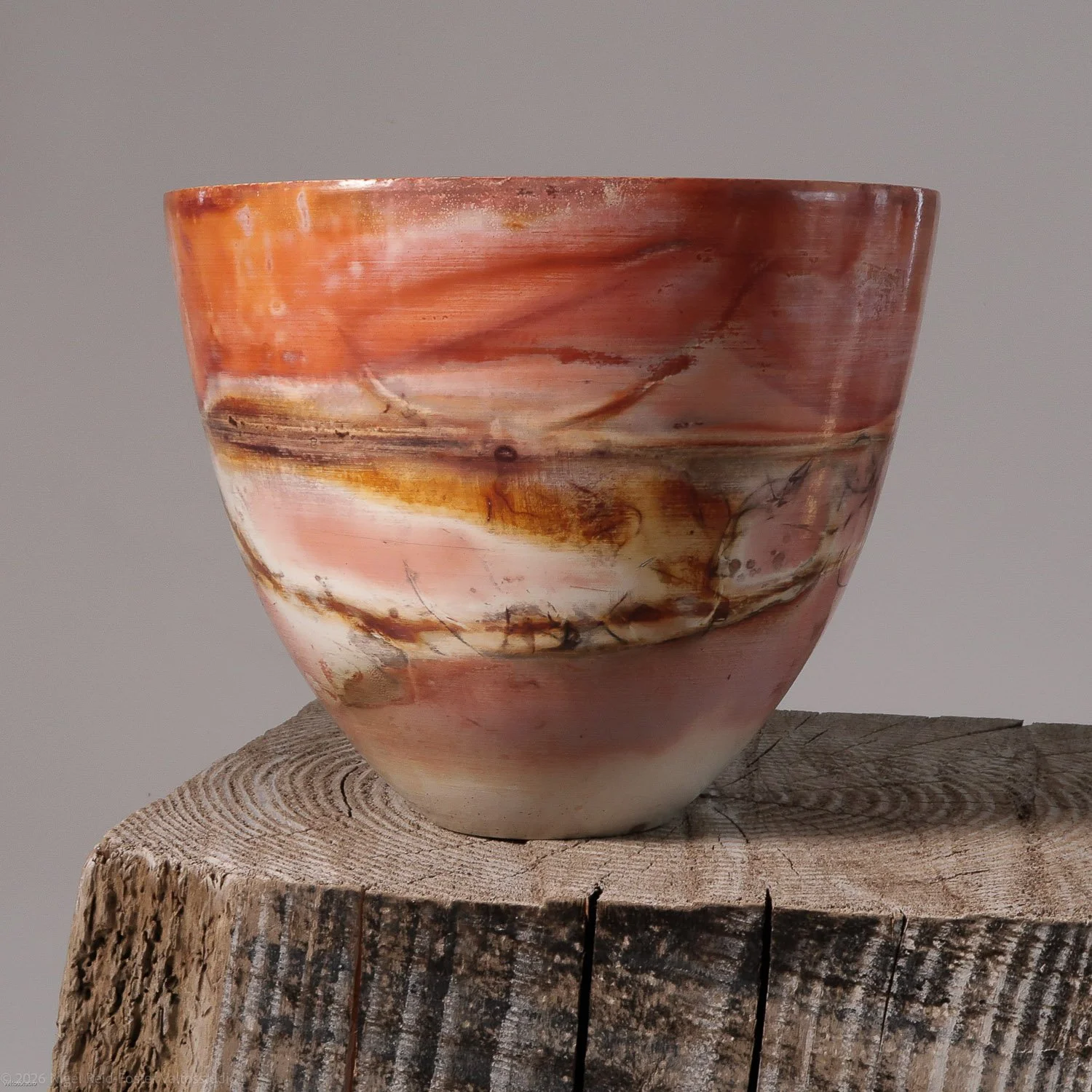 Marbled ceramic bowl with pink, white, and brown swirls resting on a weathered wooden stump.