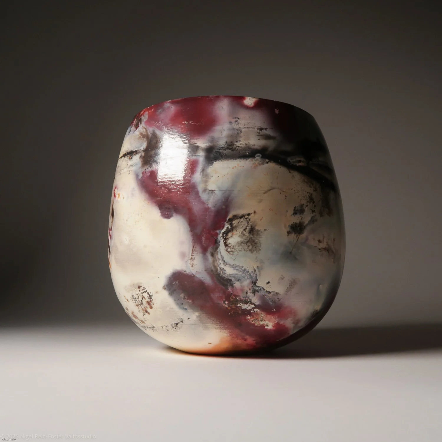 Marbled ceramic vase with swirling patterns of red, black, and white colors, placed on a plain surface against a dark background.
