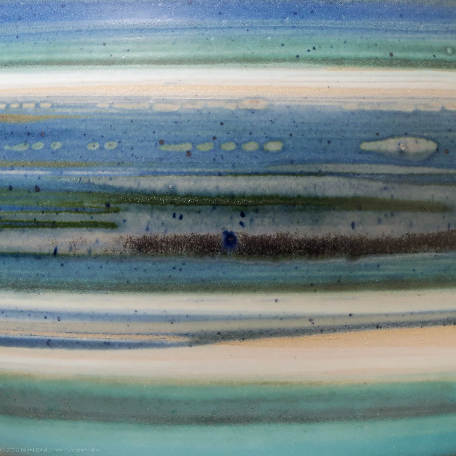 Close-up of a colorful, striped ceramic surface with horizontal streaks of blue, green, beige, and black, featuring speckles and textured details.