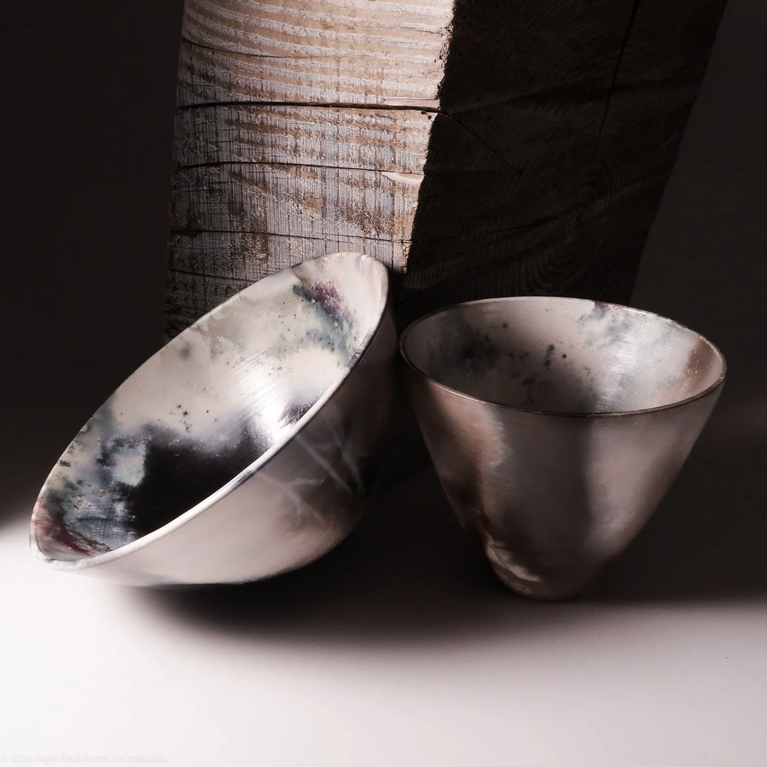 Two ceramic vessels with a rustic finish, one slightly tilted, against a dark textured wooden background.