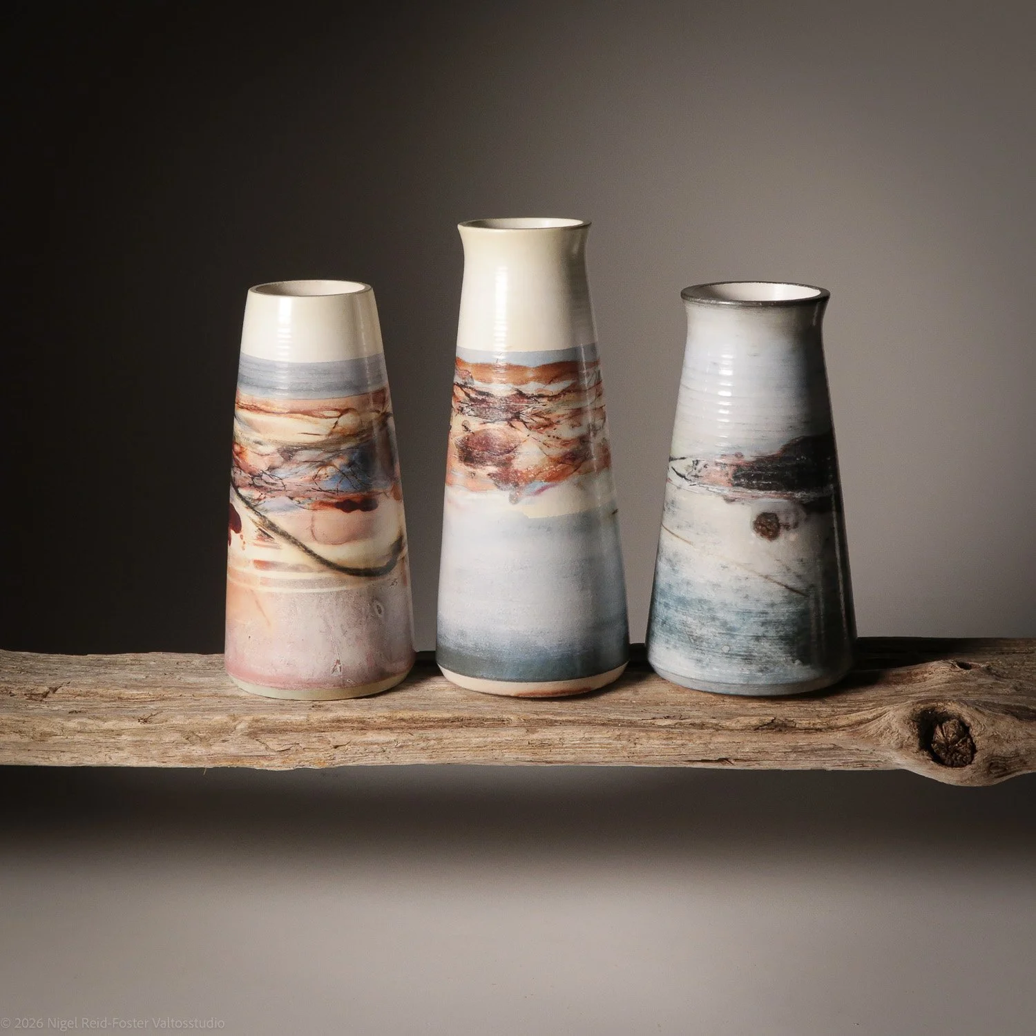 Three ceramic vases with abstract artistic designs, placed on a rustic wooden shelf.