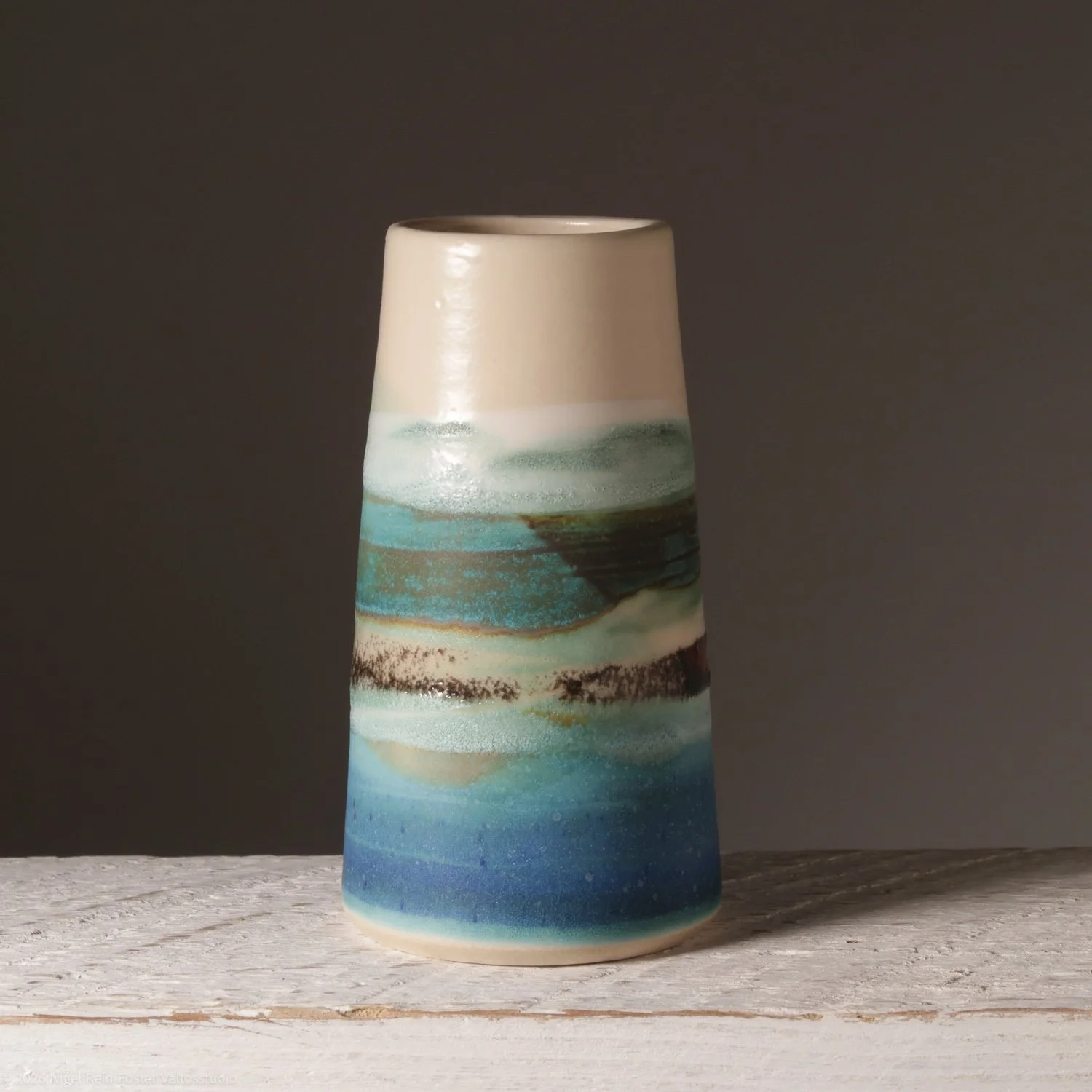 Ceramic vase with a painted landscape scene featuring waves and a rocky shoreline, placed on a wooden surface against a plain gray background.