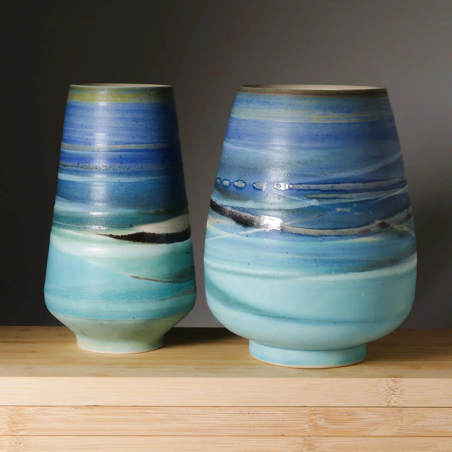 Two ceramic vases with blue, white, and black marbled patterns on a wooden surface.