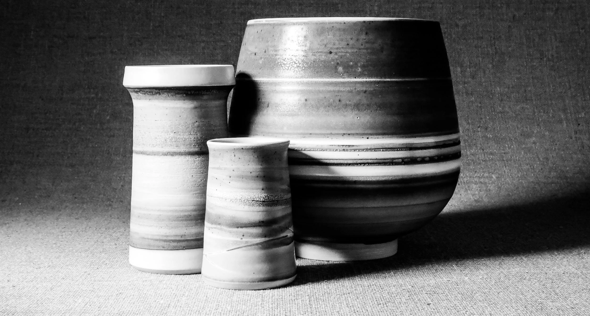 Black and white photo of five pottery vases with horizontal striped patterns, arranged from smallest to largest against a textured background.