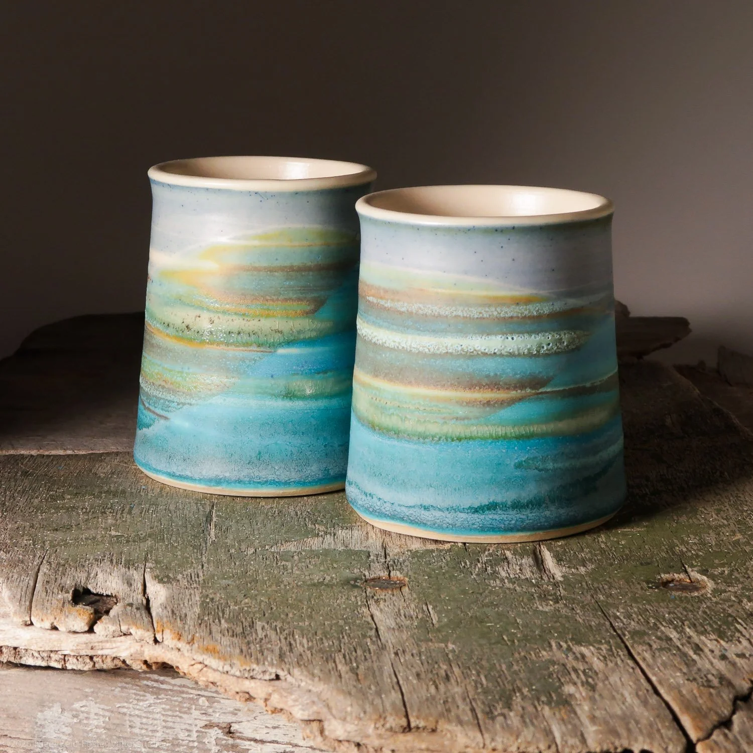 Two ceramic vases with swirling blue, green, yellow, and white glaze, placed on a weathered wooden surface.