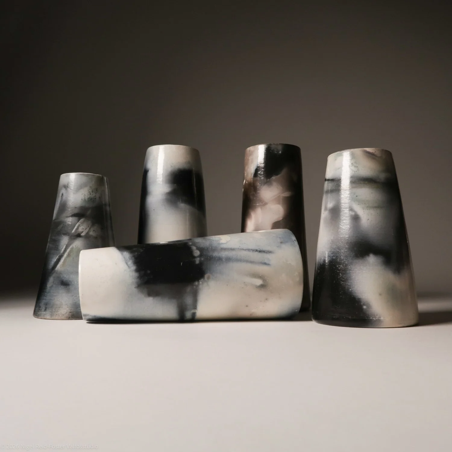 Five ceramic vessels with black, white, and gray marbled patterns on a flat surface with a dark background.