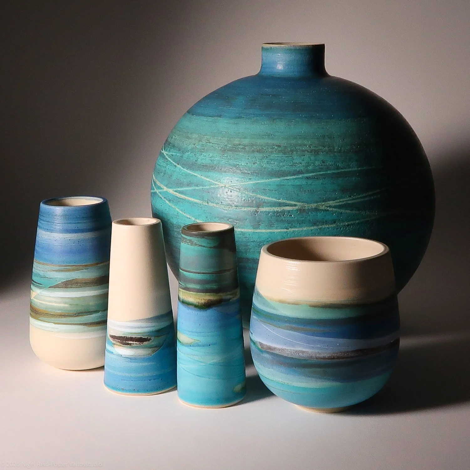 A collection of six ceramic vases with blue, green, and white abstract patterns, arranged on a neutral surface with a dark background.