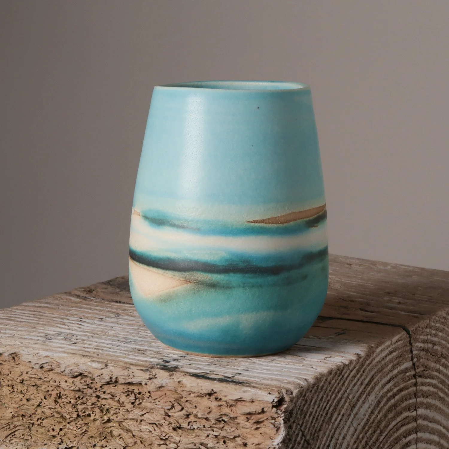 Blue ceramic vase with abstract wave-like design on a weathered wooden surface.