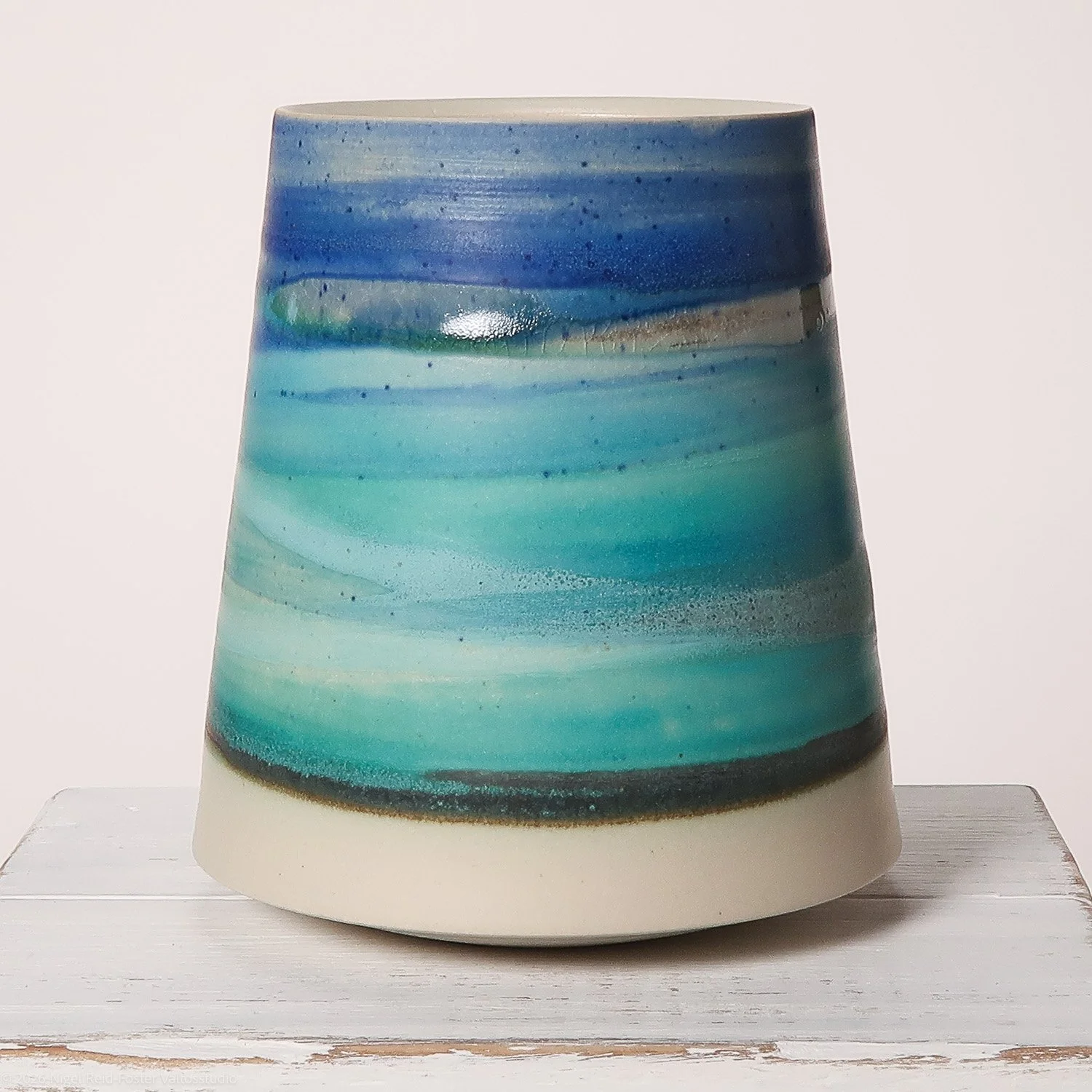 Handmade ceramic vase with a blue and turquoise wave pattern, placed on a white wooden surface.