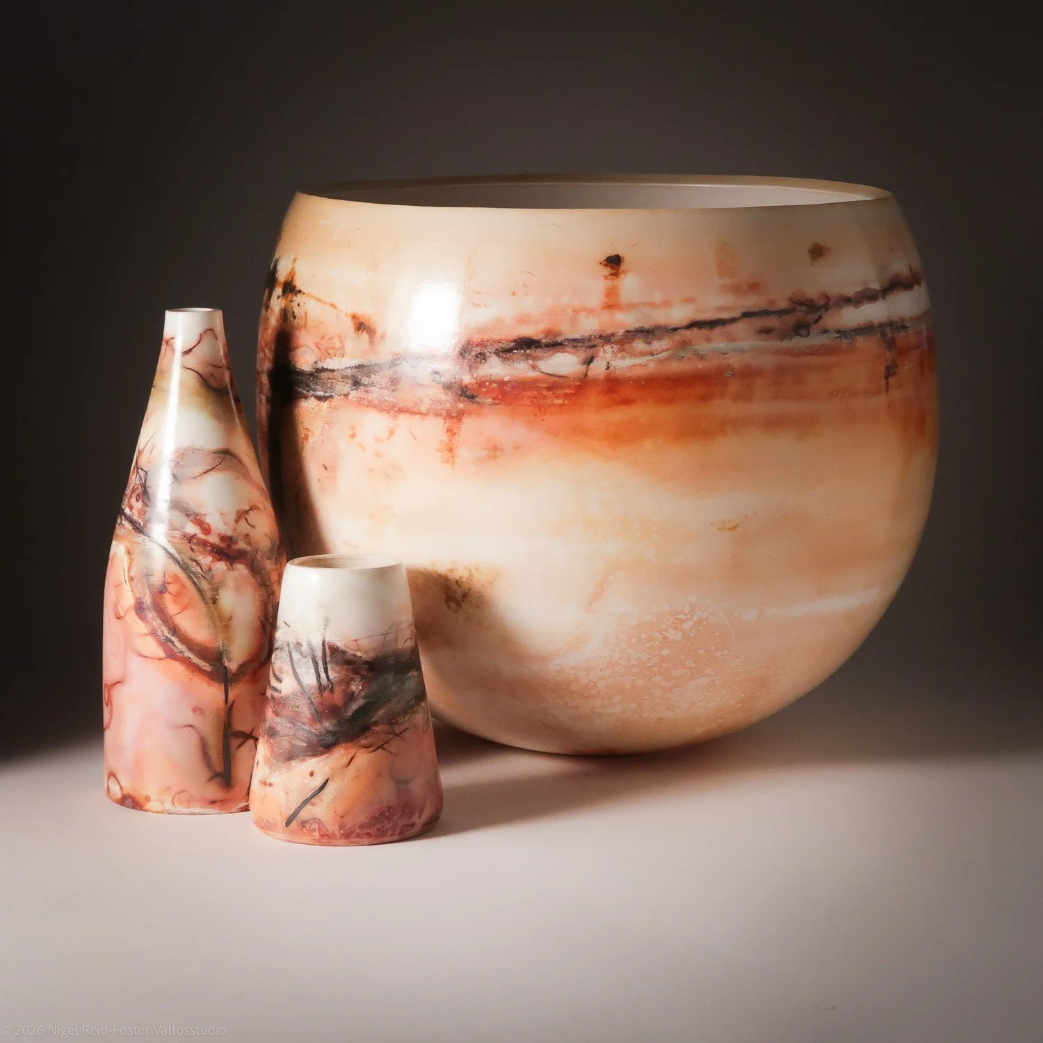Three marble-patterned pottery vessels, including a large round bowl and two smaller vases, displayed against a dark background.