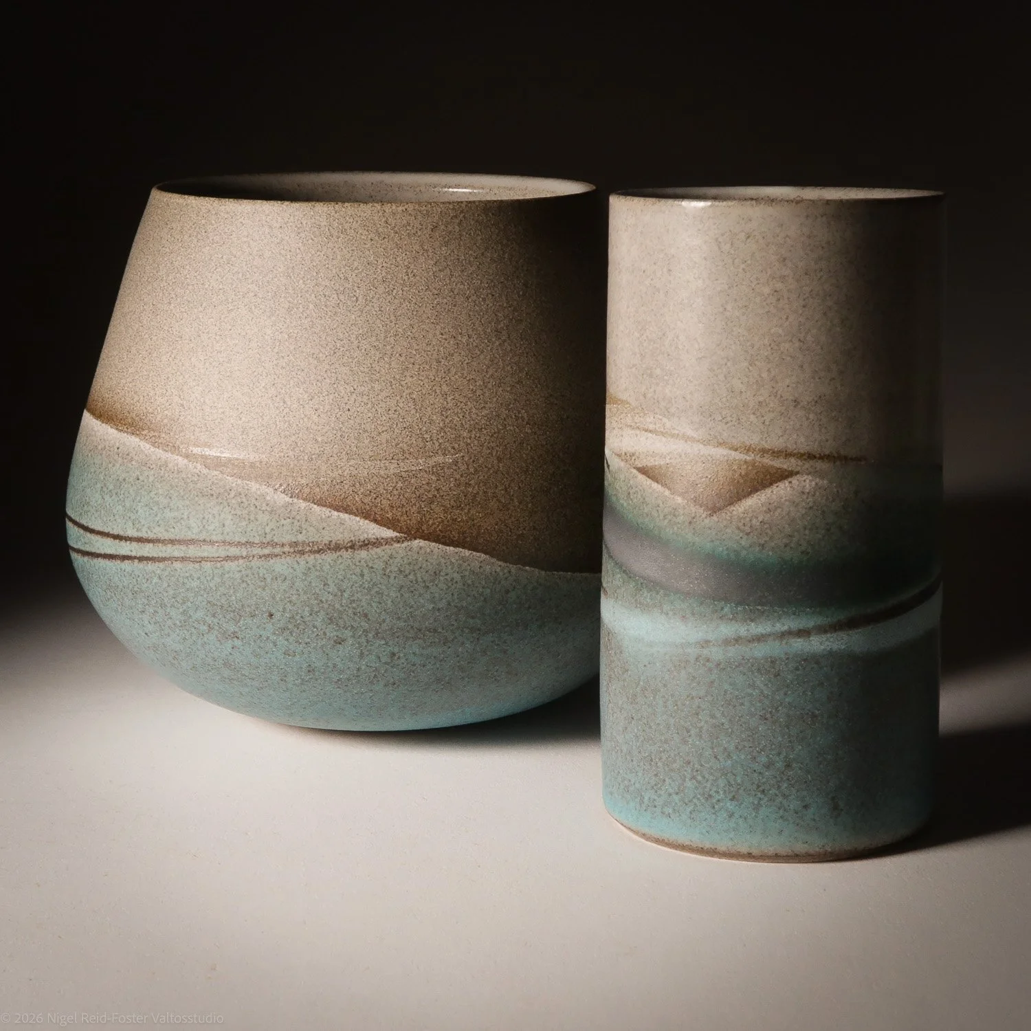 Two ceramic vases with abstract wave patterns in beige, brown, and light blue colors, placed on a white surface with a dark background.