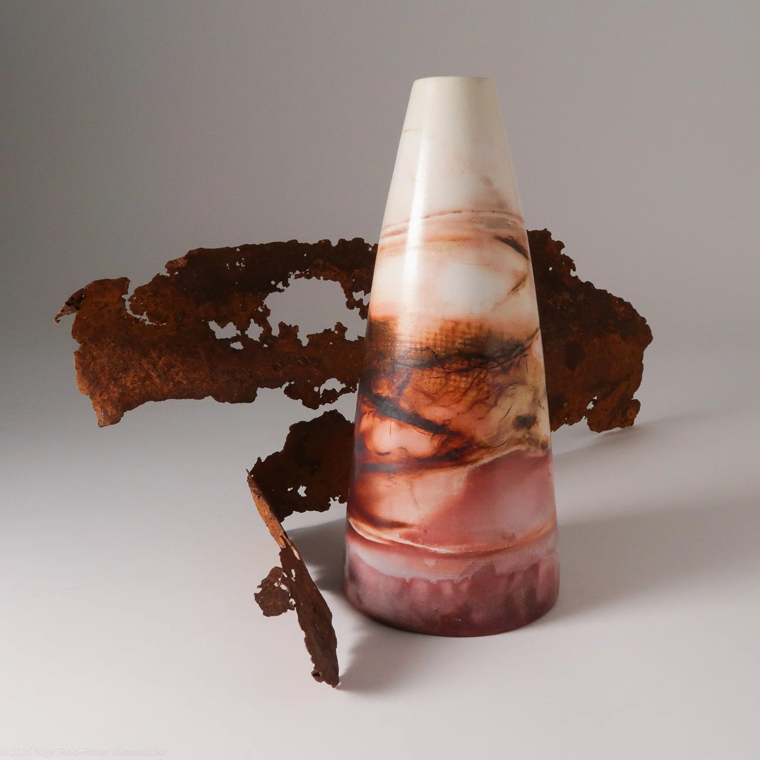 A conical marble sculpture with swirls of pink, white, and black next to a piece of rusted, perforated metal.