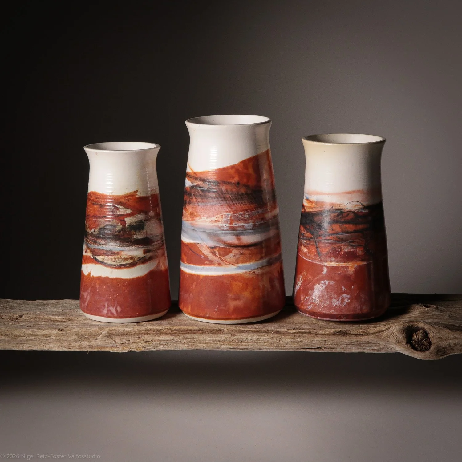 Three ceramic vases with abstract reddish-brown and black designs on a rustic wooden shelf against a dark background.