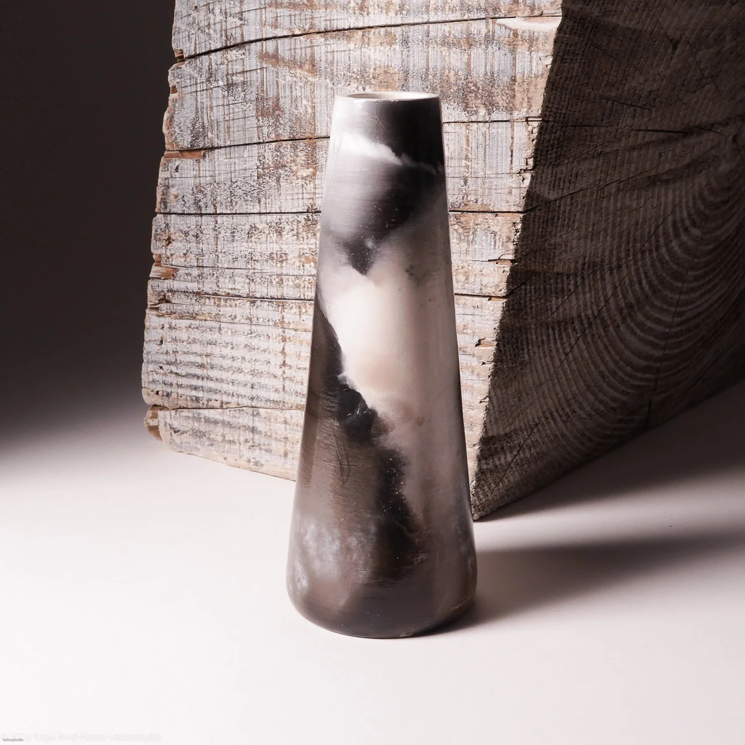 A tall, cone-shaped object with a swirling black and white pattern, placed on a white surface with a weathered wooden block in the background.