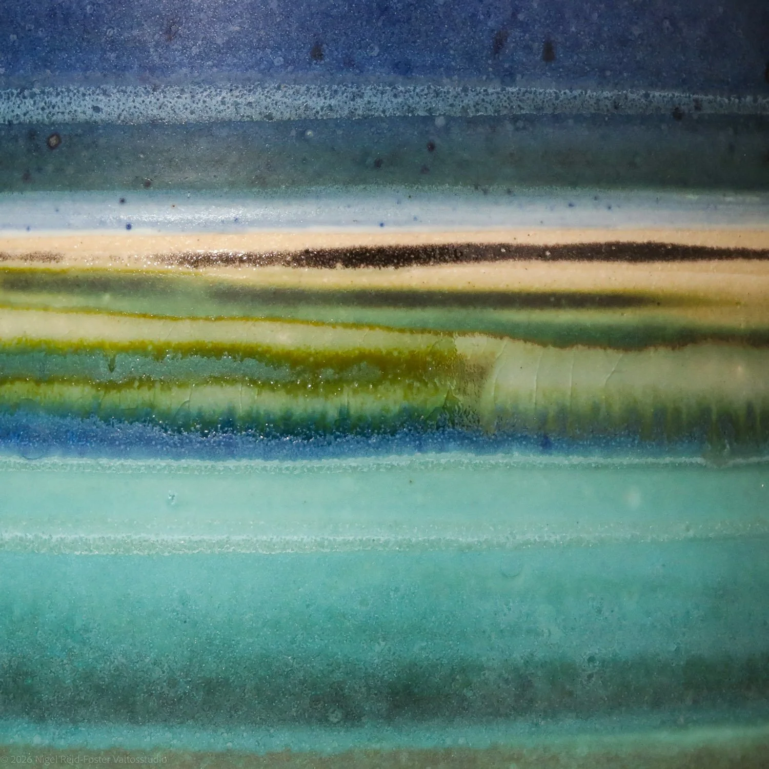 Abstract close-up of a glass surface with streaks and splatters of blue, green, black, and beige paint.