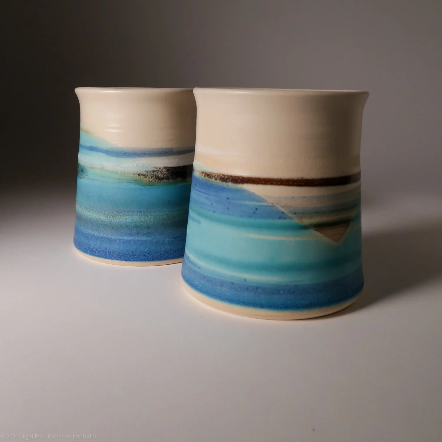 Two ceramic vessels with blue, white, and brown abstract stripe designs, set against a plain background.