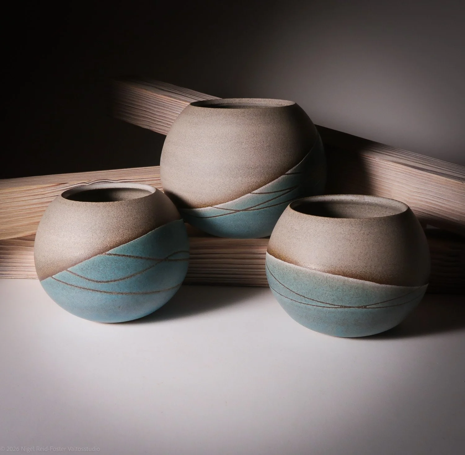 Three round ceramic vases with blue and beige wavy patterns, placed against a minimalist background with wooden accents.