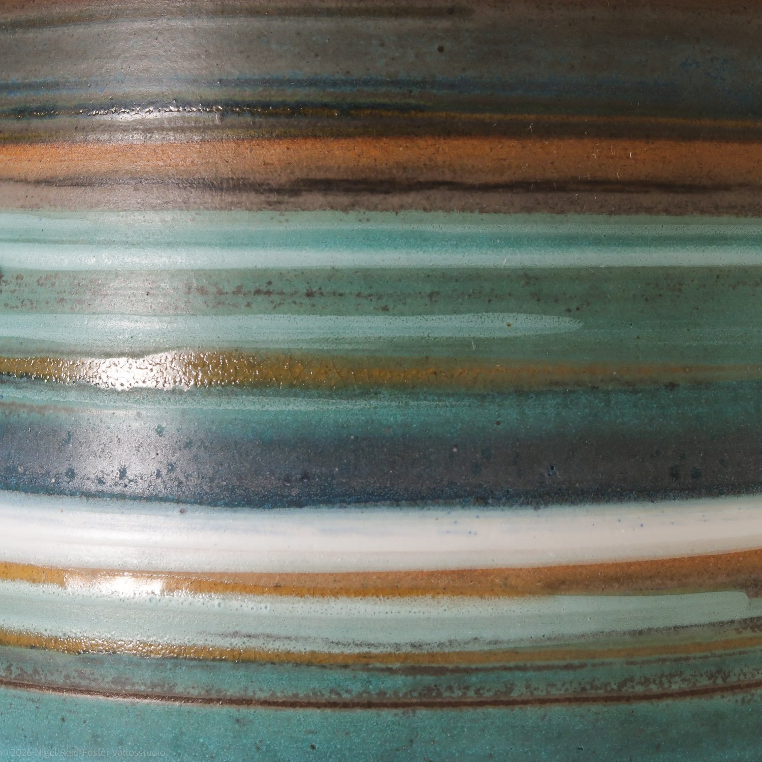 Close-up photo of a ceramic object with horizontal bands of earthy colors including brown, teal, white, and black, with a glossy finish.